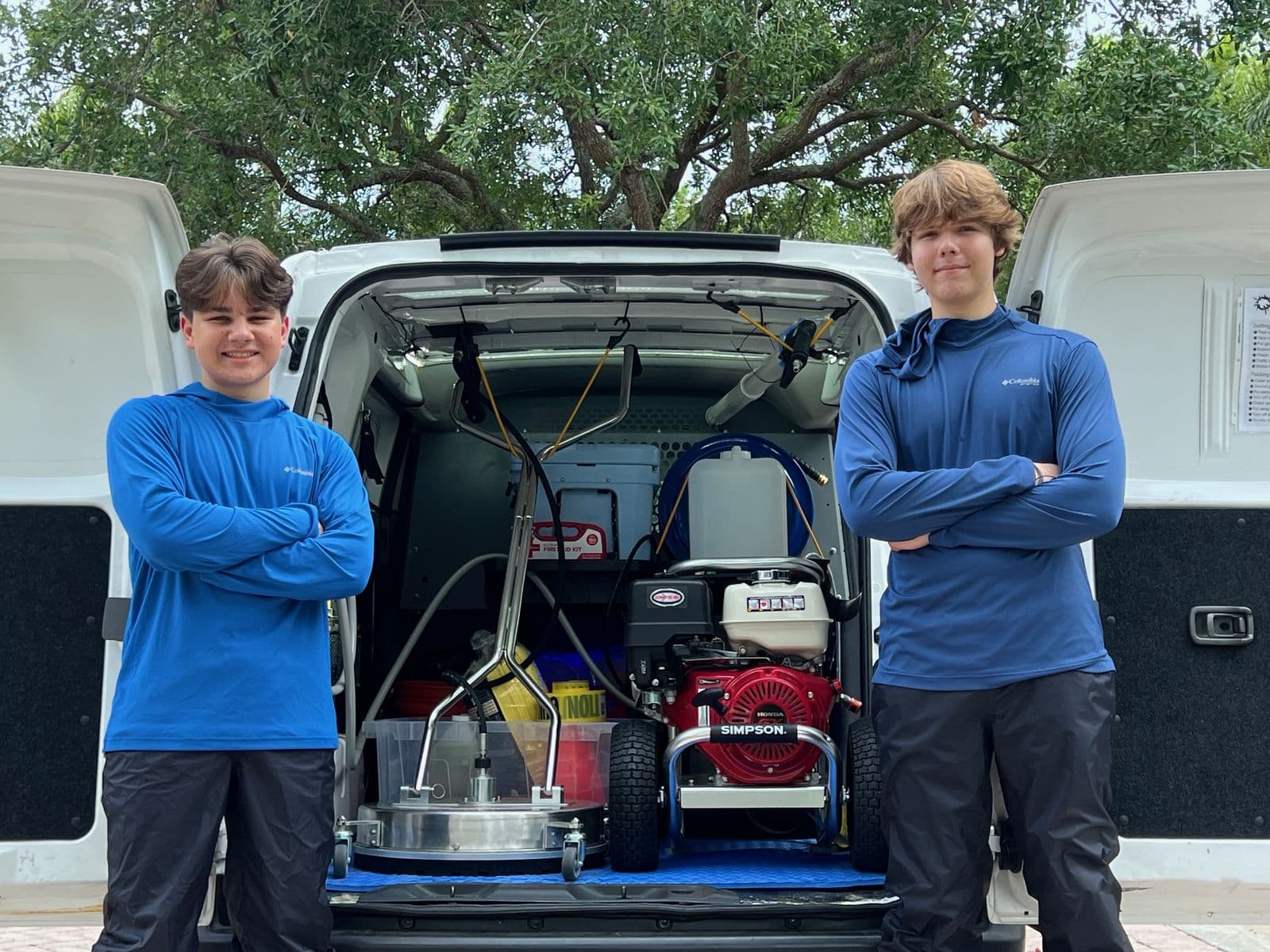 Julius Ivsan and Gleb Labzov standing with arms crossed at the open rear doors of the Panther Power Clean van, pressure washer and surface cleaner loaded behind them