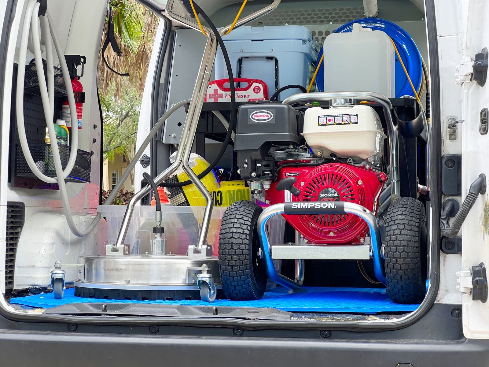 The open rear of the van showing a Simpson pressure washer with a Honda engine, a surface cleaner, hose reels, a water tank, and a first-aid kit